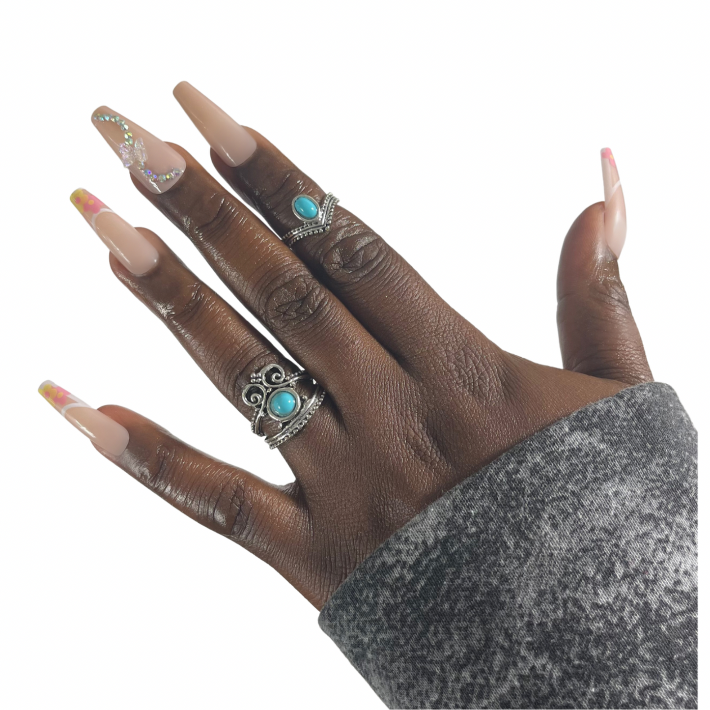 Model Wearing Casket Ready Beauty's Coffin-shaped long-length glossy nude pink nails with accent nails with white tips, pink and yellow flowers, rhinestones, and butterfly gems.