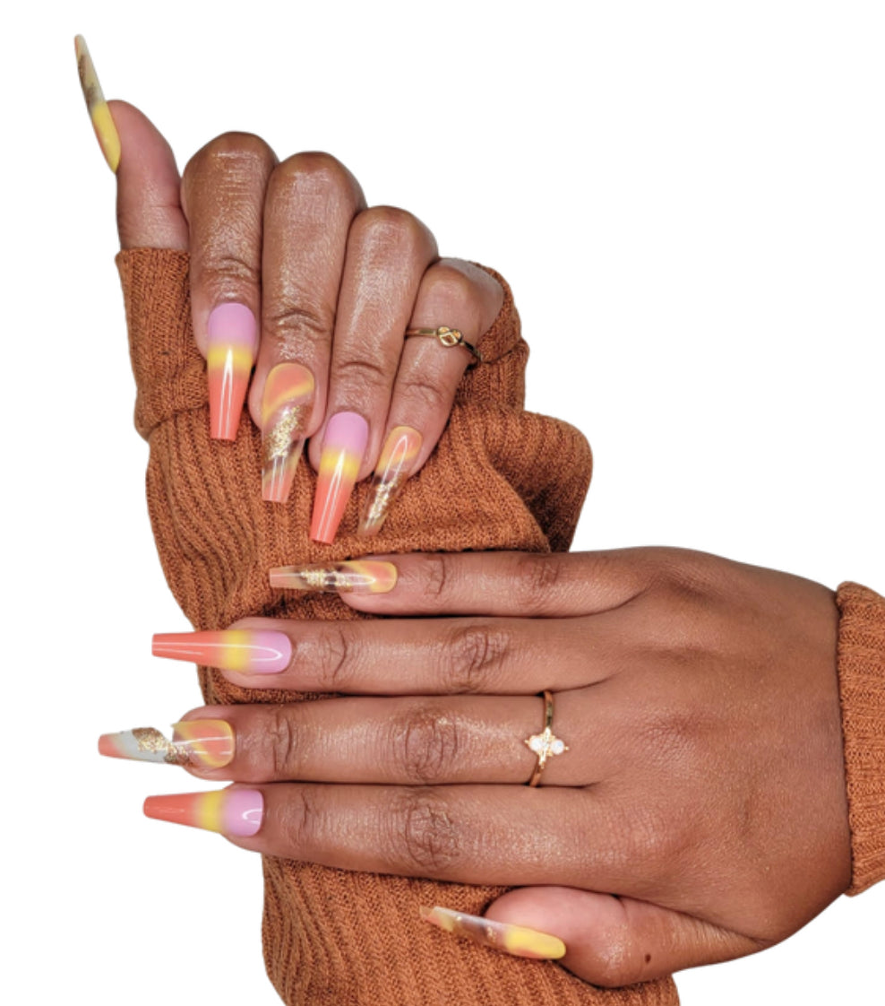 Model Wearing Casket Ready Beauty's Coffin-shaped long-length glossy sunset pink, yellow, and orange nails, with decorated accent nails with clear and gold glitter. 